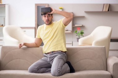 Genç erkek öğrenci evde sanal gözlüklerle eğleniyor.