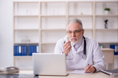 Yaşlı erkek doktor hastanede hap öneriyor.