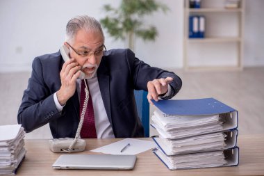 Old employee speaking by phone at workplace