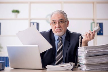 Old employee speaking by phone at workplace