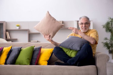 Evde bir sürü yastığı olan yaşlı bir adam.