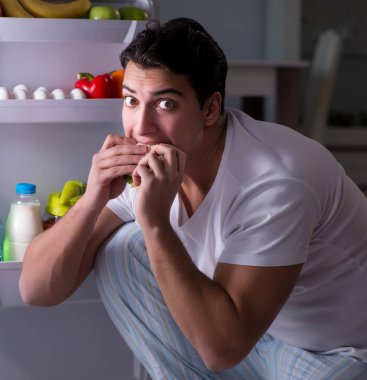 Buzdolabının başındaki adam gece yemek yiyor.