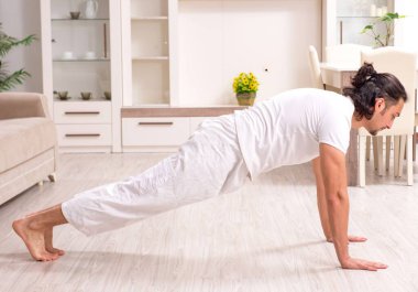 Genç adam evde fiziksel egzersiz yapıyor.