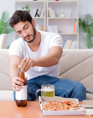 Pizza yiyen adam evde yemek yiyor, dinleniyor.