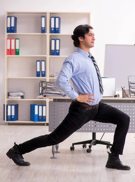 The young handsome male employee doing exercises in the office