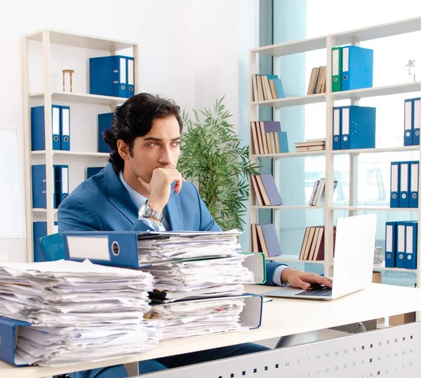 The young handsome male employee with too much work in the office