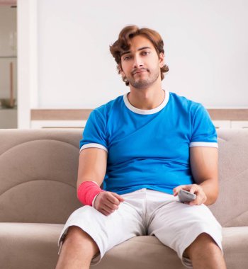 Kolu yaralı genç adam kanepede oturuyor.