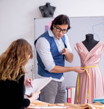 Genç erkek terzi kız öğrenciye öğretmenlik yapıyor.