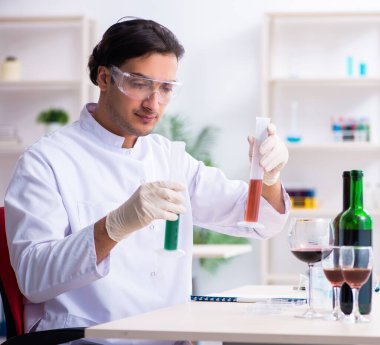 Erkek kimyager laboratuvarda şarap örneklerini inceliyor.