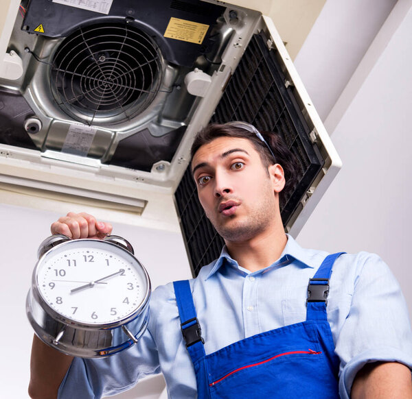 Молодой ремонтник ремонтирует потолочный кондиционер