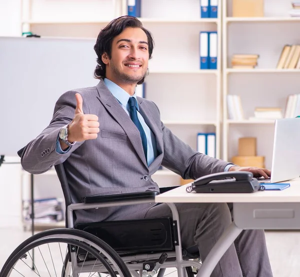 The young handsome employee in wheelchair at the office