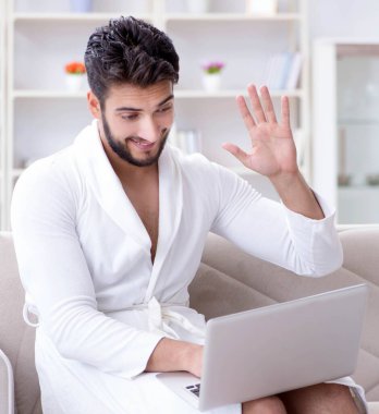 Genç adam evde dizüstü bilgisayarla çalışıyor.