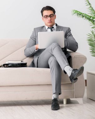 Dizüstü bilgisayarı olan iş adamı kanepede oturuyor.