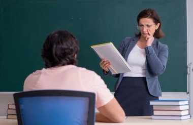 Sınıftaki yaşlı bayan öğretmen ve erkek öğrenci.