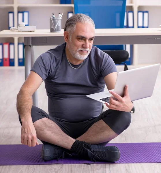 The white bearded old man employee doing exercises in the office