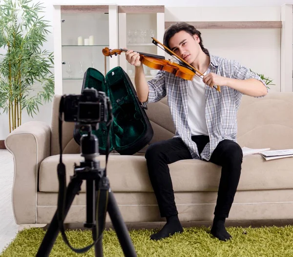 The young male blogger playing violin at home