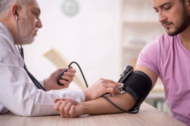 Genç hastaların tansiyonunu ölçen yaşlı bir doktor.