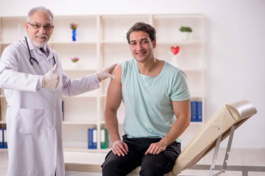 Genç hasta yaşlı erkek doktoru aşı konseptiyle ziyaret ediyor.