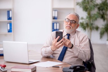 Old employee speaking by phone at workplace