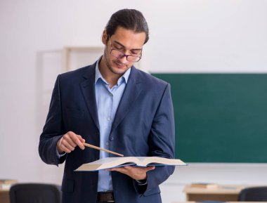 Genç öğretmen yeşil panonun önünde.