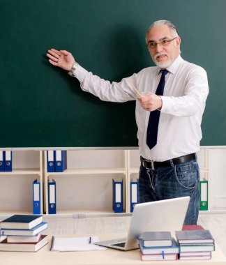 Tahtanın önündeki yaşlı erkek öğretmen.