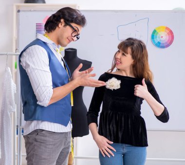 Genç erkek terzi bayan müşteriyle konuşuyor.