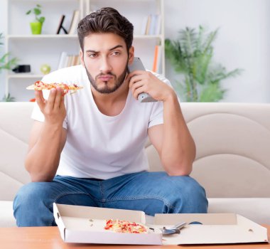 Pizza yiyen adam evde yemek yiyor, dinleniyor.