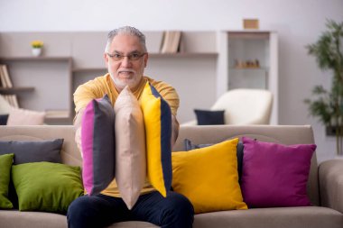 Evde bir sürü yastığı olan yaşlı bir adam.