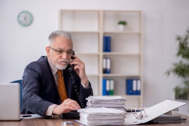 Old employee speaking by phone at workplace