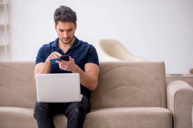 Evde kredi kartı tutan genç bir adam.
