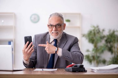 Old employee speaking by phone at workplace