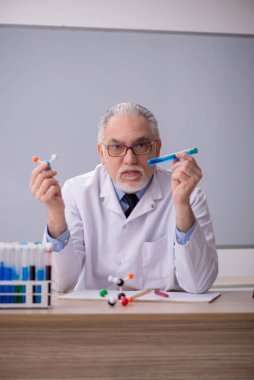 Old chemist teacher sitting in the classroom