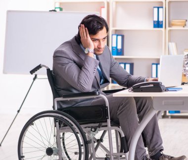 The young handsome employee in wheelchair at the office