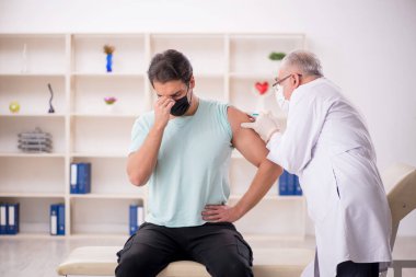 Genç hasta yaşlı erkek doktoru aşı konseptiyle ziyaret ediyor.