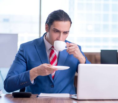 Genç yakışıklı işadamı ofiste oturuyor.