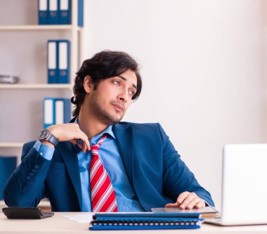 Genç yakışıklı işadamı ofiste oturuyor.