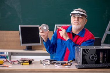 Sınıfta bilgisayar tamir eden yaşlı bir erkek tamirci.