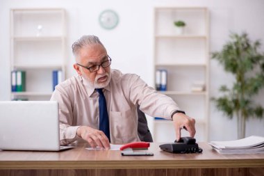 Old employee speaking by phone at workplace