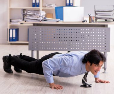 The young handsome male employee doing exercises in the office