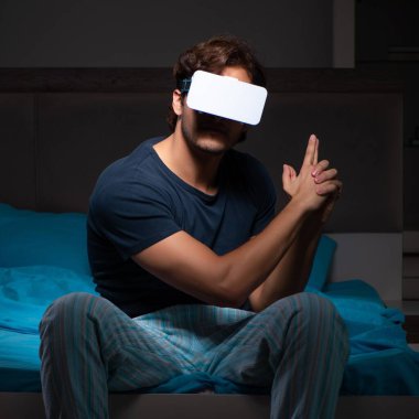 Genç adam gece yatağında bilgisayar oyunları oynuyor.