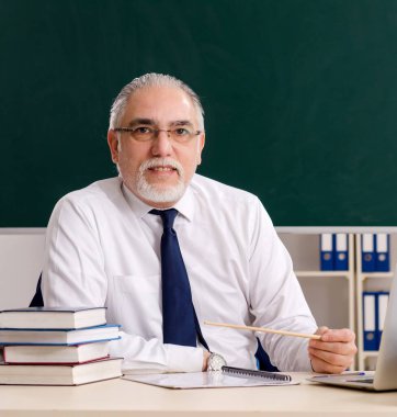 Tahtanın önündeki yaşlı erkek öğretmen.