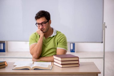 Sınıfta beyaz tahtanın önünde oturan genç öğrenci.