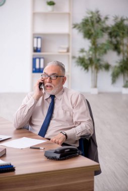 Old employee speaking by phone at workplace
