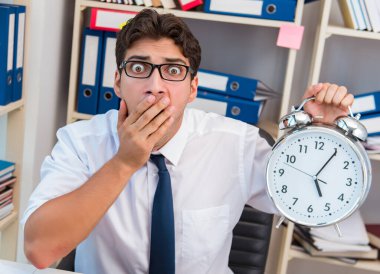 Ofiste evrak ve kitap yığınlarıyla çalışan bir işadamı.