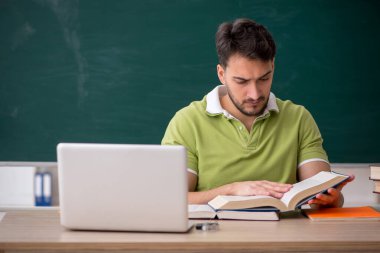 Genç öğrenci yeşil panonun önünde oturuyor.