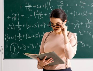 Kadın öğretmen karatahtanın önünde duruyor.