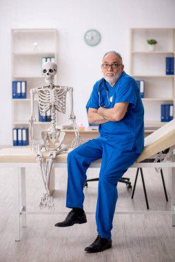 Yaşlı doktor hastanede iskeleti inceliyor.