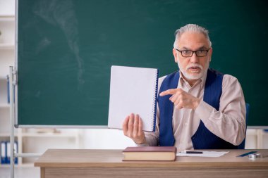 Eski öğretmen yeşil panonun önünde.