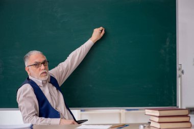 Eski öğretmen yeşil panonun önünde.