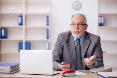 Old employee speaking by phone at workplace